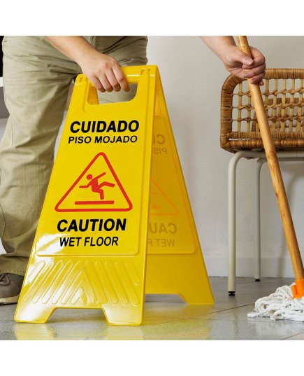 Trabajador de mantenimiento en Arequipa secando un piso cerca de un cartel de precaución suelo resbaladizo señal universal.